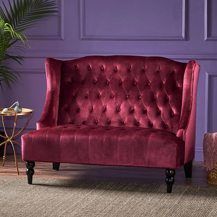 Wine red velvet wingback loveseat styled against a purple paneled wall.