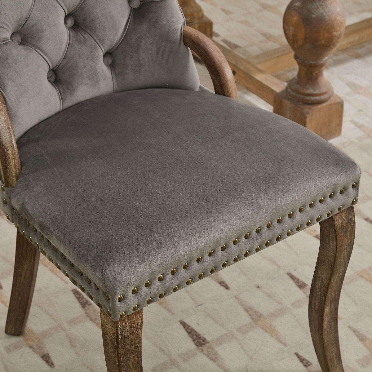 Gray velvet dining chair with a tufted back, wood handle, and curved wood legs