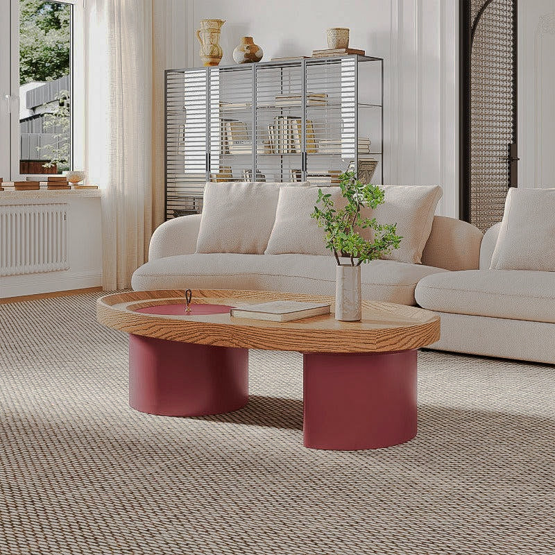 Oval wood-look coffee table with red cylindrical supports beside a cream sofa