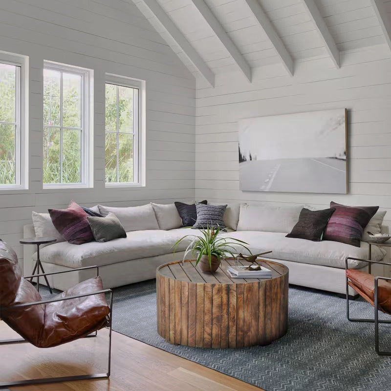 Round plank-style drum coffee table in a bright living room with white sofas